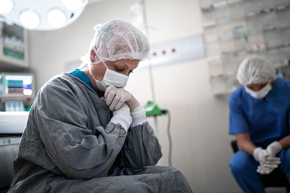 A woman in a hospital gown sits on a chair, appearing contemplative in a medical setting.