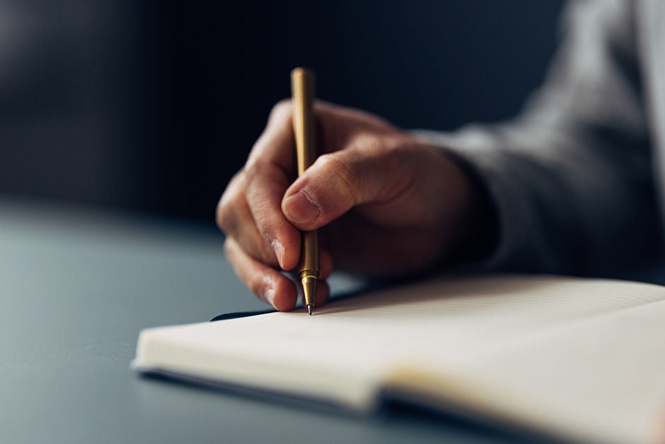 A hand holding a pen writing on a notebook.