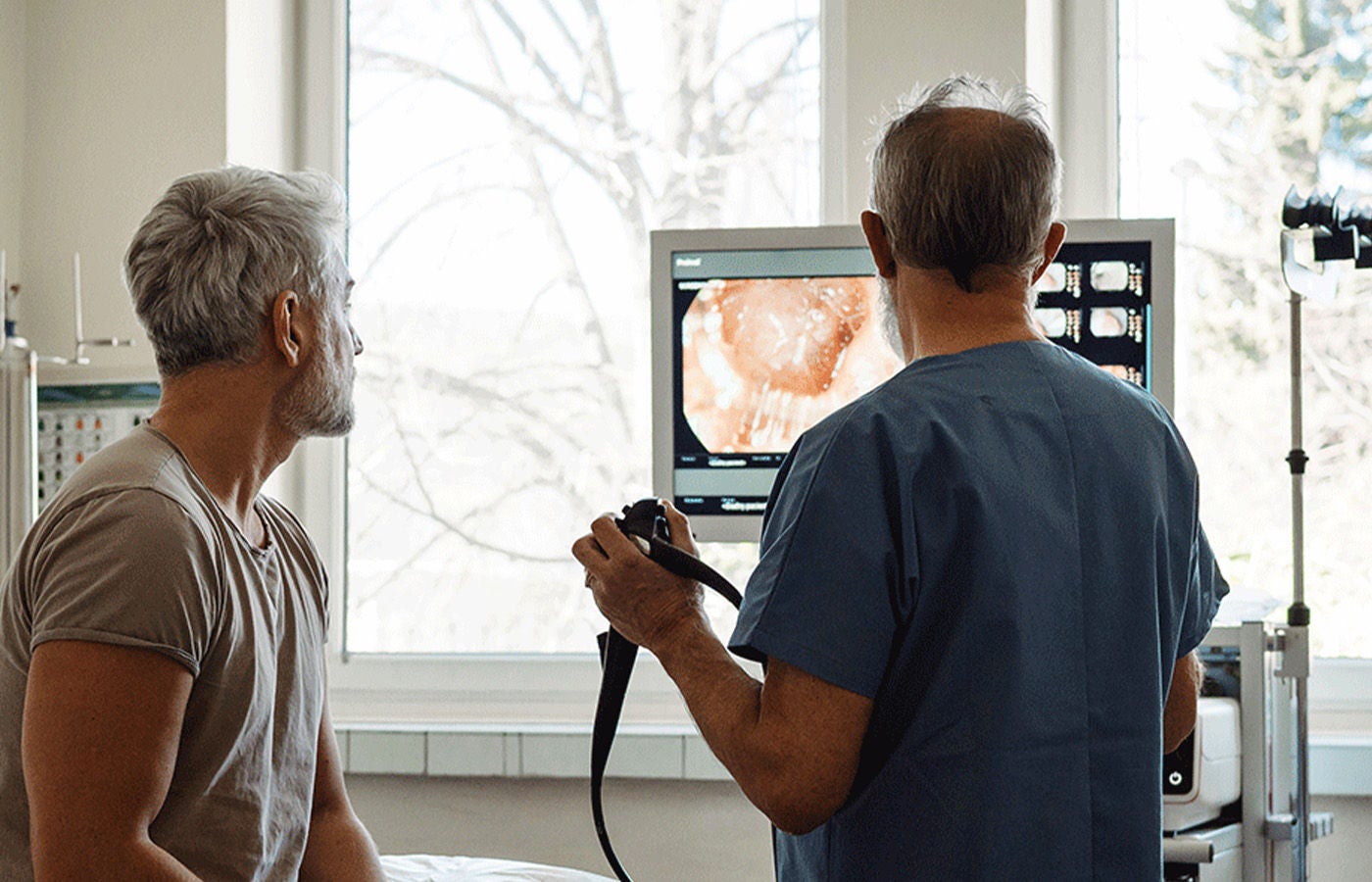 A doctor in scrubs showing a patient internal imaging results on a medical monitor during a clinical consultation