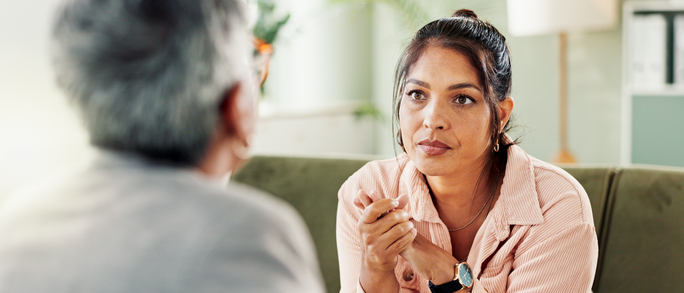 A woman in serious conversation with an older person while seated on a sofa, suggesting a sensitive or important family discussion.