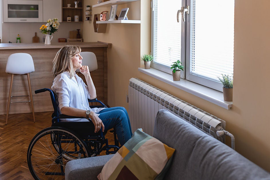 A women sitting on a wheelchair, looking outside the window.