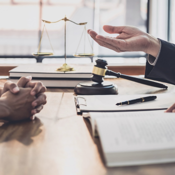 Two people facing each other at a lawyers desk, only their hands and documents and items on the desk visible