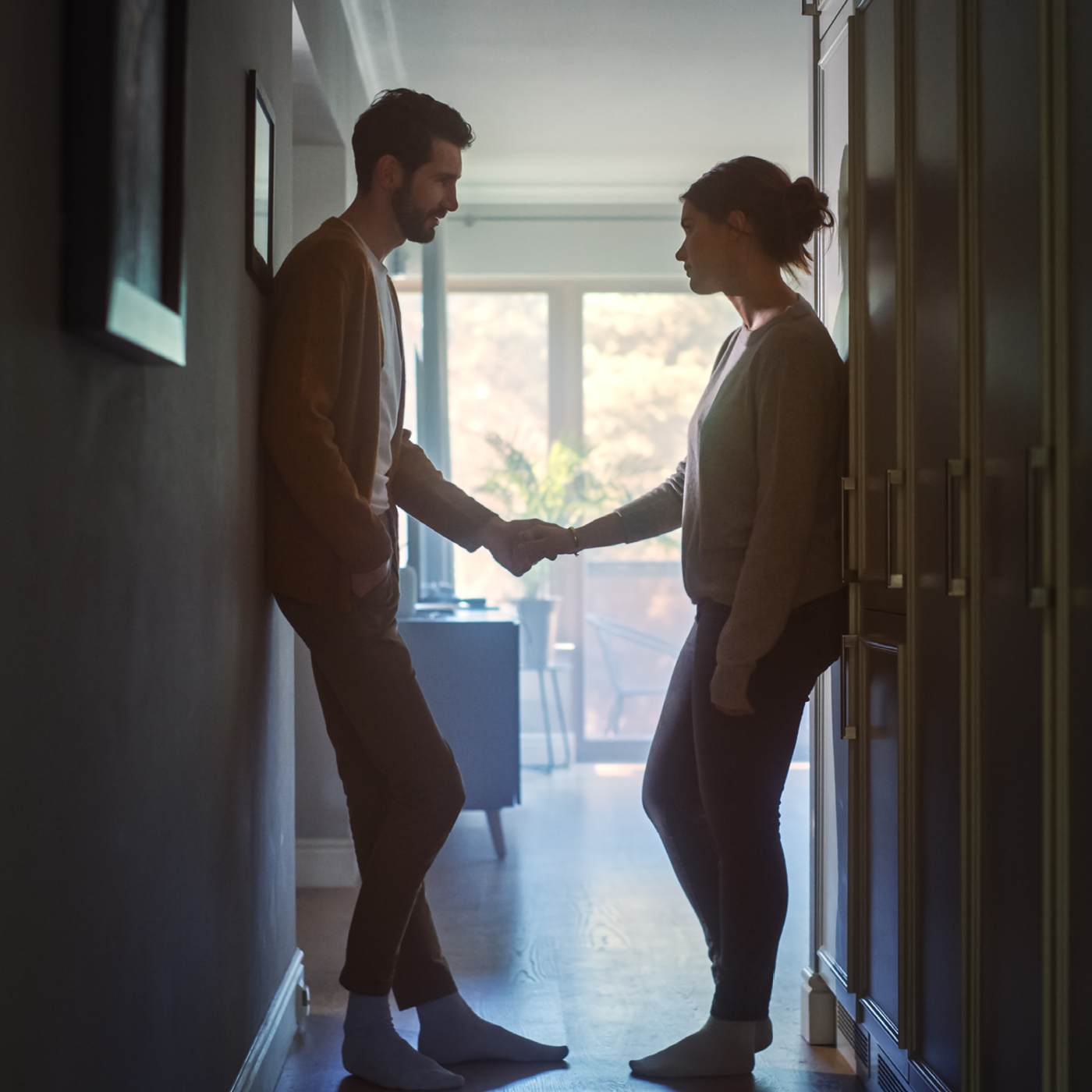 Two people holding hands in a hallway at home, conveying a moment of connection or reconciliation.