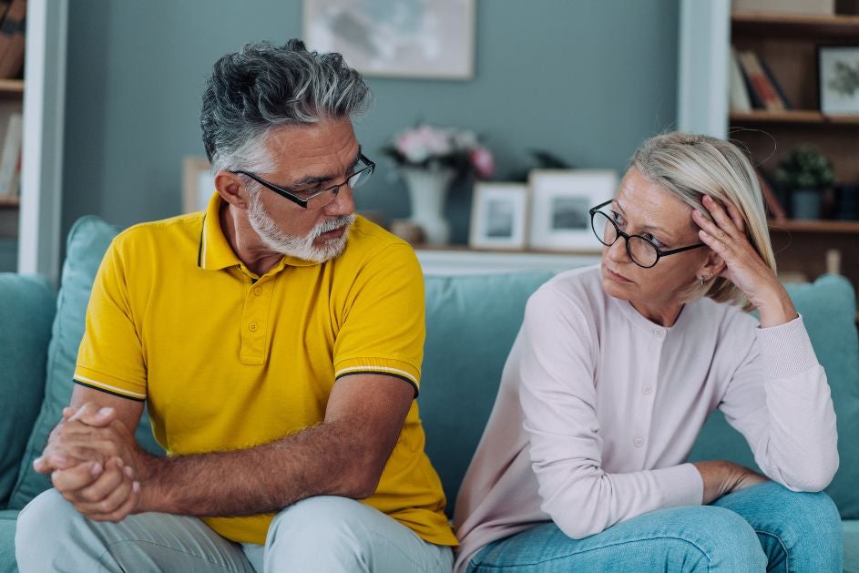 A senior couple sits comfortably on a couch, engaged in conversation and sharing a warm moment.