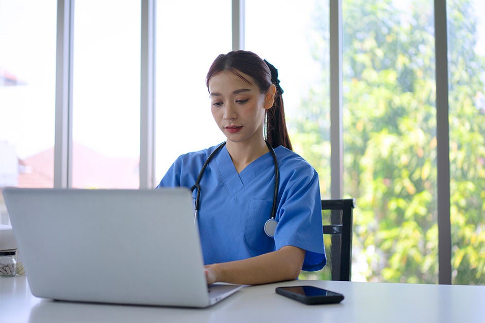 A doctor sitting by the window, working on her laptop.