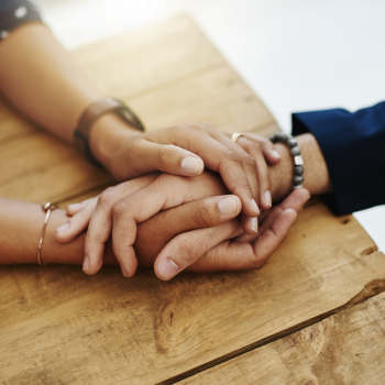 Two people holding hands at a table with only their hands visible
