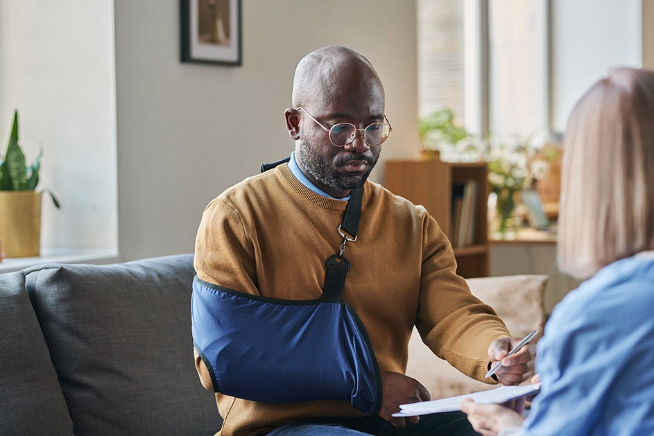A man with a broken arm sits on a couch, talking to a medical professional.
