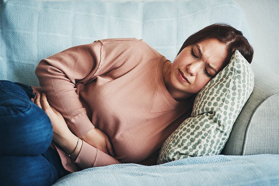 A woman lies on a couch, holding her stomach in pain, with a distressed expression on her face.