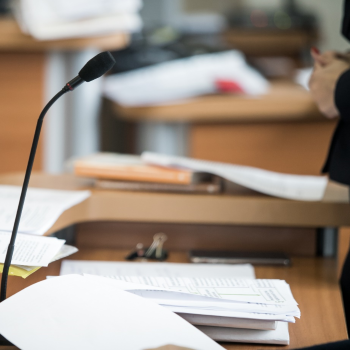 A lectern with many papers stacked on top and a microphone