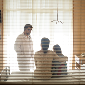 In a doctors office, a doctor speaks with two people sitting on a bed in the doctor's office