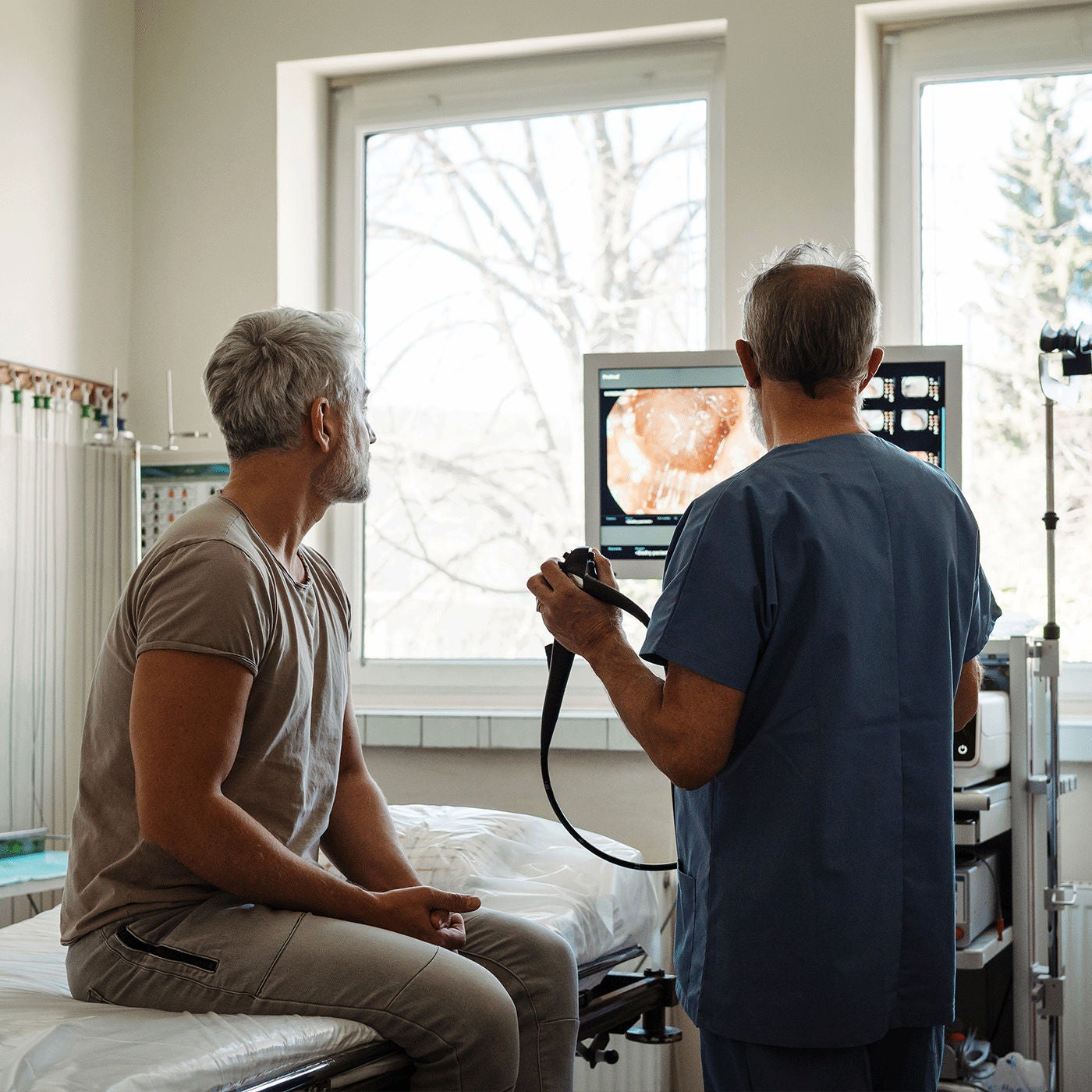 A doctor in scrubs showing a patient internal imaging results on a medical monitor during a clinical consultation