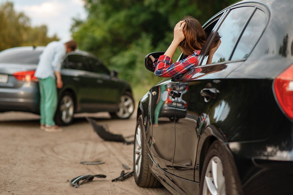A woman examines her damaged car after it was involved in an accident, showing concern on her face.