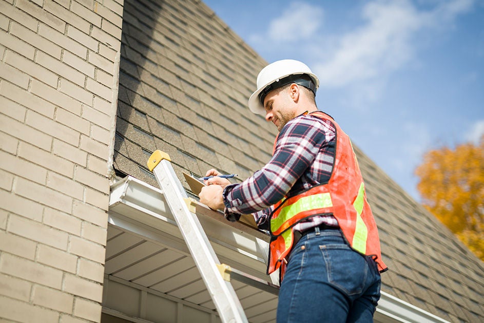 A man on a ladder inspecting the roof of a house for maintenance or repairs.