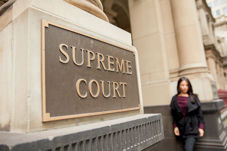  A woman stands in front of a sign reading "Supreme Court"