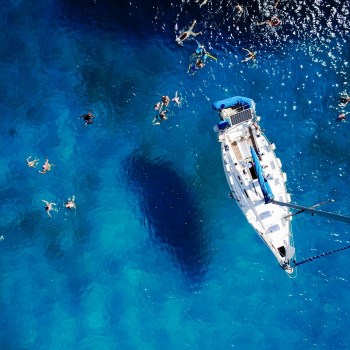 A birds eye view of a yacht on blue water with people swimming