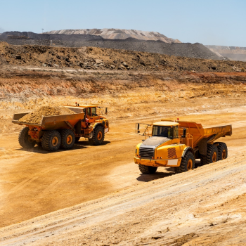 Two large trucks in the outback with piles of sand in their trays