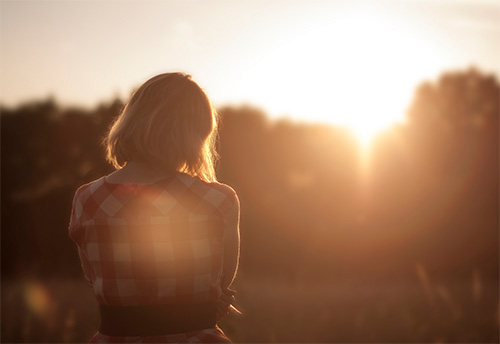 A woman standing in a field at sunset