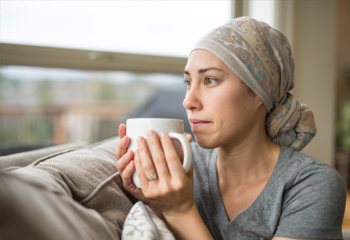 A woman unable to work due to illness sitting on the couch with a cup of tea