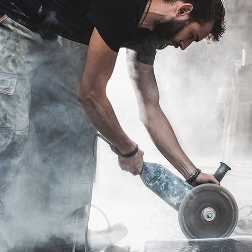 man holding a saw cutting stone, surrounded by dust