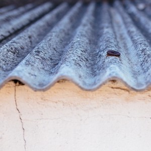 Close-up of a weathered corrugated metal roof with a small rusted hole, resting on a cracked, cream-coloured wall.