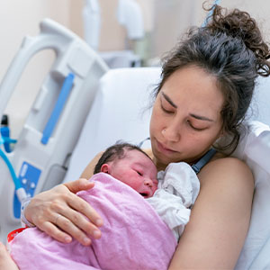 A woman cradles her newborn in a hospital bed, smiling gently as she embraces her child.