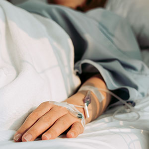 A patient lying in a hospital bed with an IV drip in their hand, suggesting medical treatment or care.