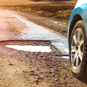 A car navigating a bumpy road filled with potholes, highlighting the uneven surface and potential driving hazards.