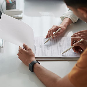 Two people reviewing and signing documents at a desk, suggesting a financial or legal consultation.