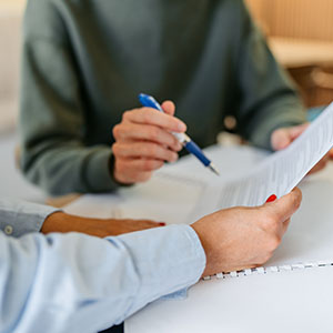 Two people reviewing and signing documents at a desk, suggesting a financial or legal consultation.