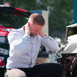 A man holding his neck in pain while crouching beside a damaged car following a road accident