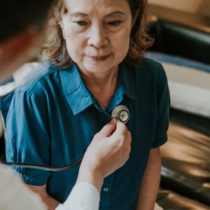 Doctor listening to an older woman’s chest with a stethoscope during a home consultation