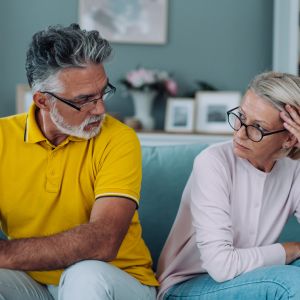 A senior couple sits comfortably on a couch, engaged in conversation and sharing a warm moment.