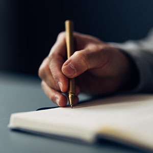 A hand holding a pen writing on a notebook.