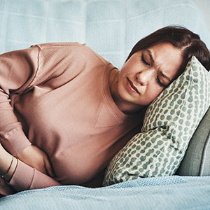 A woman lies on a couch, holding her stomach in pain, with a distressed expression on her face.