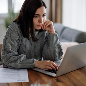 A woman working on a laptop at a table, appearing engaged and thoughtful.