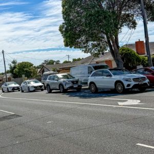Cars parked along the roadside in a quiet residential neighborhood, surrounded by houses and greenery.