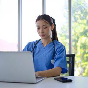 A doctor sitting by the window, working on her laptop.