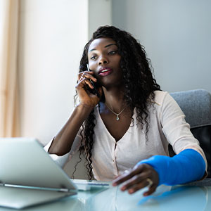 A woman wearing a wrist brace sits at a desk, focused on her laptop while working.