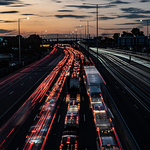 A long-exposure night shot of heavy traffic on a Melbourne freeway at dusk, with streaks of light from passing vehicles.