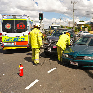 Emergency responders attending a two-car collision at an intersection, with an ambulance at the scene.