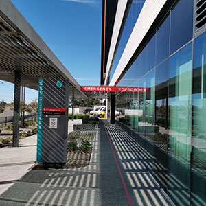 department. Glass walls reflect sunlight. An ambulance is visible in the distance.