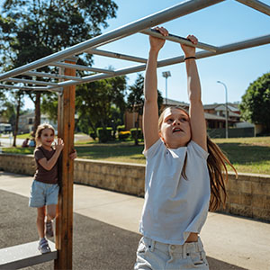 Two children playing on monkey bars at an outdoor playground on a sunny day.