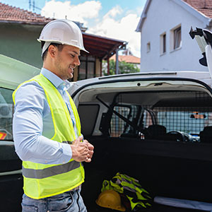 A construction worker in a hard hat and vest stands next to a van.