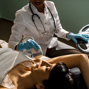 A doctor performs an ultrasound on a reclining patient, guiding the probe across her abdomen beside a console.