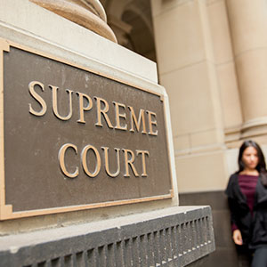 A woman stands in front of a sign reading "Supreme Court"