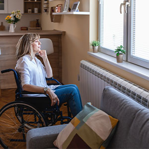 A women sitting on a wheelchair, looking outside the window.