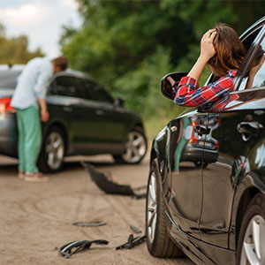 A woman examines her damaged car after it was involved in an accident, showing concern on her face.