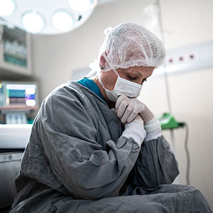 A woman in a hospital gown sits on a chair, appearing contemplative in a medical setting.