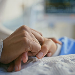 A caregiver gently holds the hand of a patient lying in a hospital bed, conveying support and compassion.