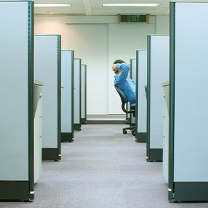 A person in a blue shirt leans back in an office chair in a row of empty cubicles.